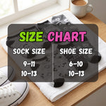 A size chart graphic overlaid on a folded pair of black patterned socks laid on a white towel on a wooden table, with a coffee cup and white sneakers nearby. The chart reads 'SIZE CHART' and lists sock sizes 9-11 / 10-13 and shoe sizes 6-10 / 10-13.