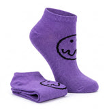 A pair of purple ankle socks with a black wavy line smiley face graphic, shown with one sock folded and one sock standing upright on a white background.