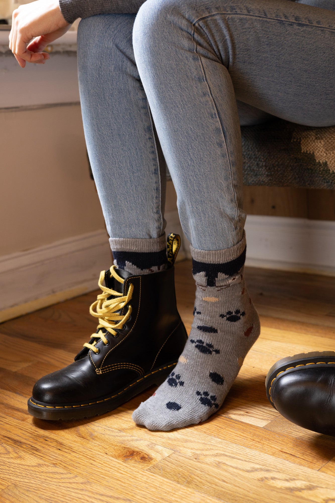 Person wearing black boots with yellow laces and gray pants, sitting on a wooden floor.