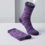 Purple crew socks with white and gray wavy stripes, shown with one sock on a clear mannequin foot and a stack of folded socks on a light gray surface.