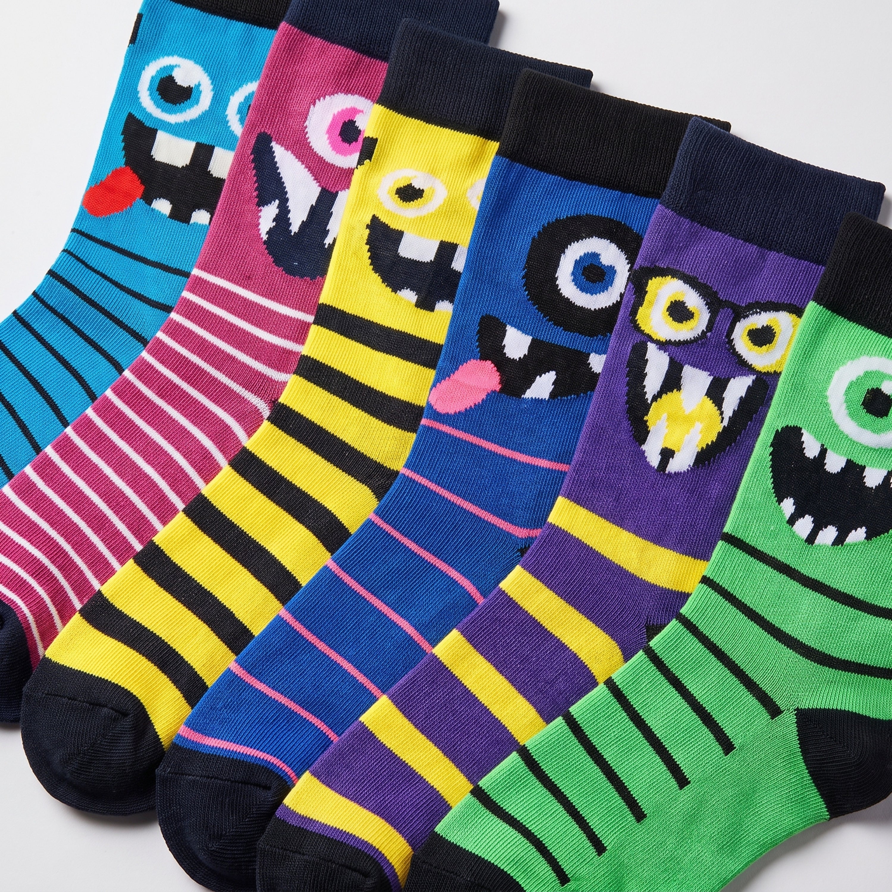 Five pairs of colorful novelty socks with cartoon monster faces, arranged diagonally on a light gray background.