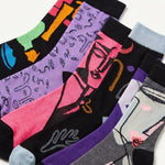A set of six patterned crew socks arranged diagonally on a white background, featuring various colorful abstract and graphic designs on black, purple, pink, gray, and light blue socks.