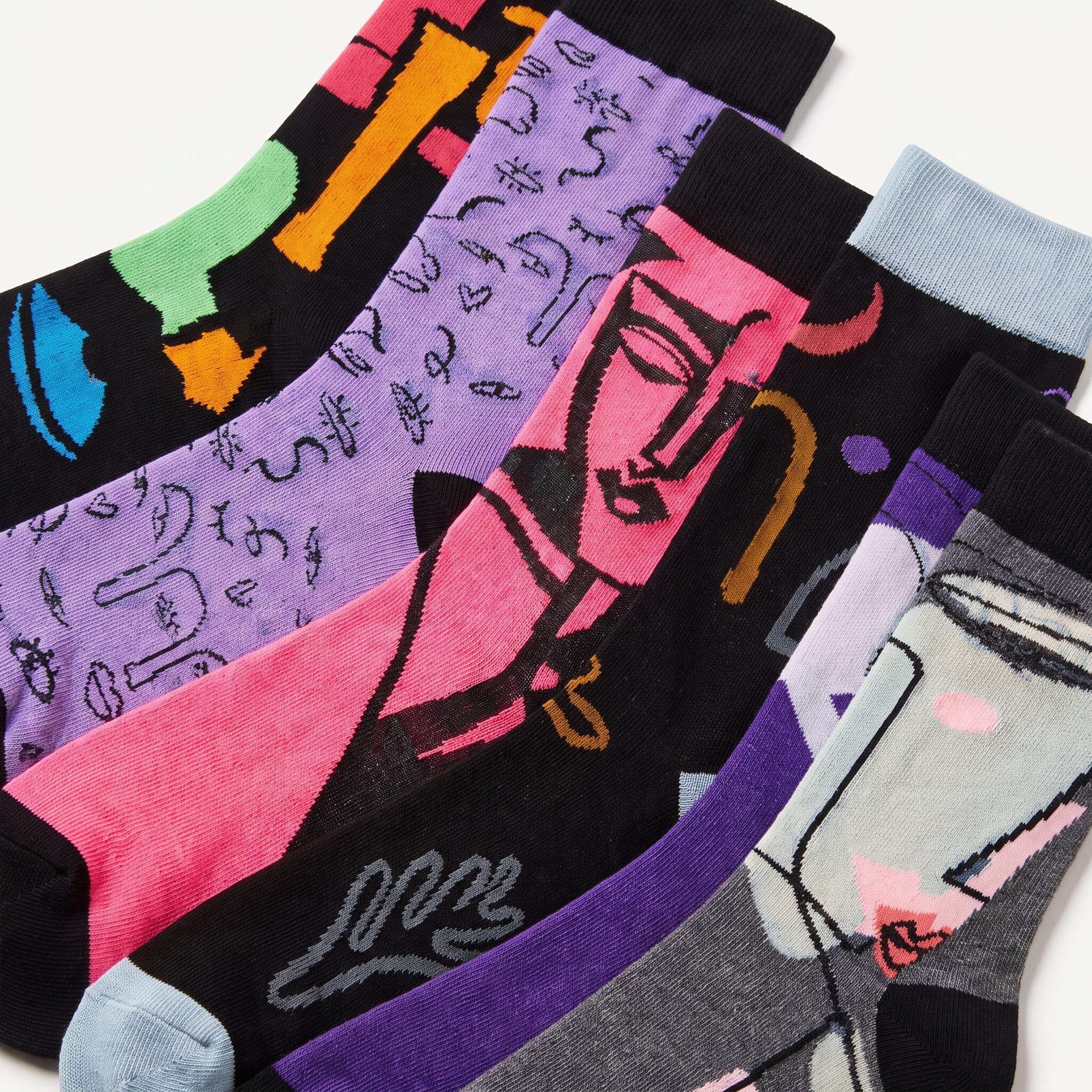 A set of six patterned crew socks arranged diagonally on a white background, featuring various colorful abstract and graphic designs on black, purple, pink, gray, and light blue socks.