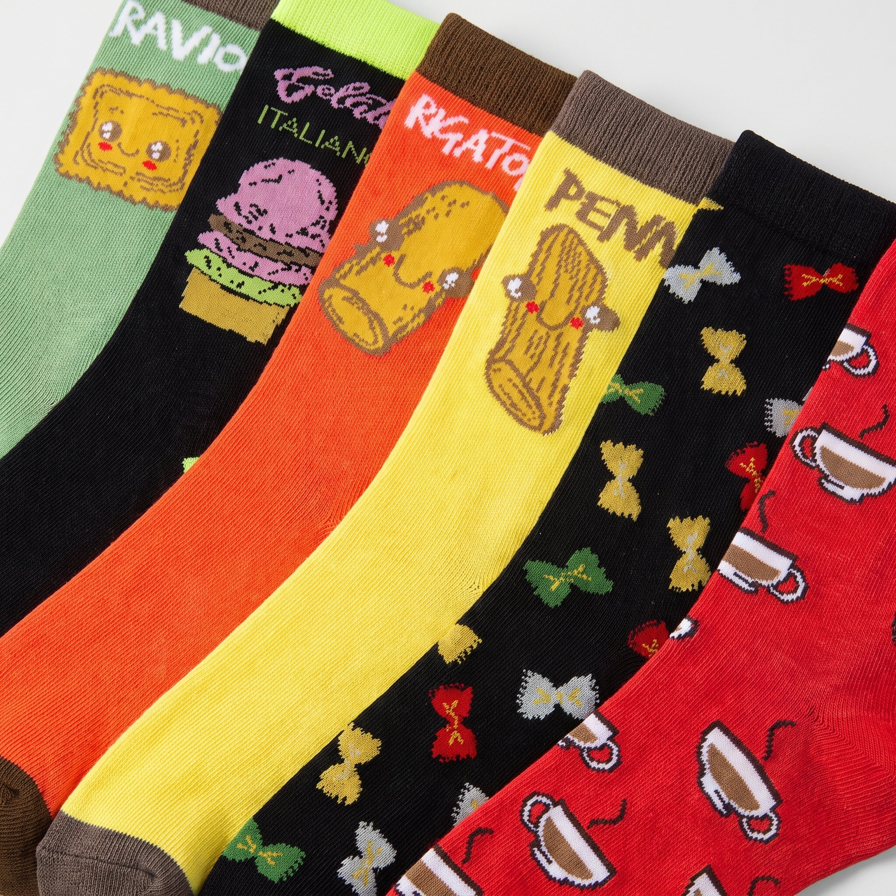 Six colorful novelty socks arranged in a fan-like layout, each with a different bright base color and pasta-themed graphic. The visible designs include a green square with a face, a black burger with 'Gelato ITALIANO' text, an orange pasta shape with 'RIGATO' text, a yellow log graphic with 'PENA' text, a black bow-tie pattern, and a red coffee cup pattern.