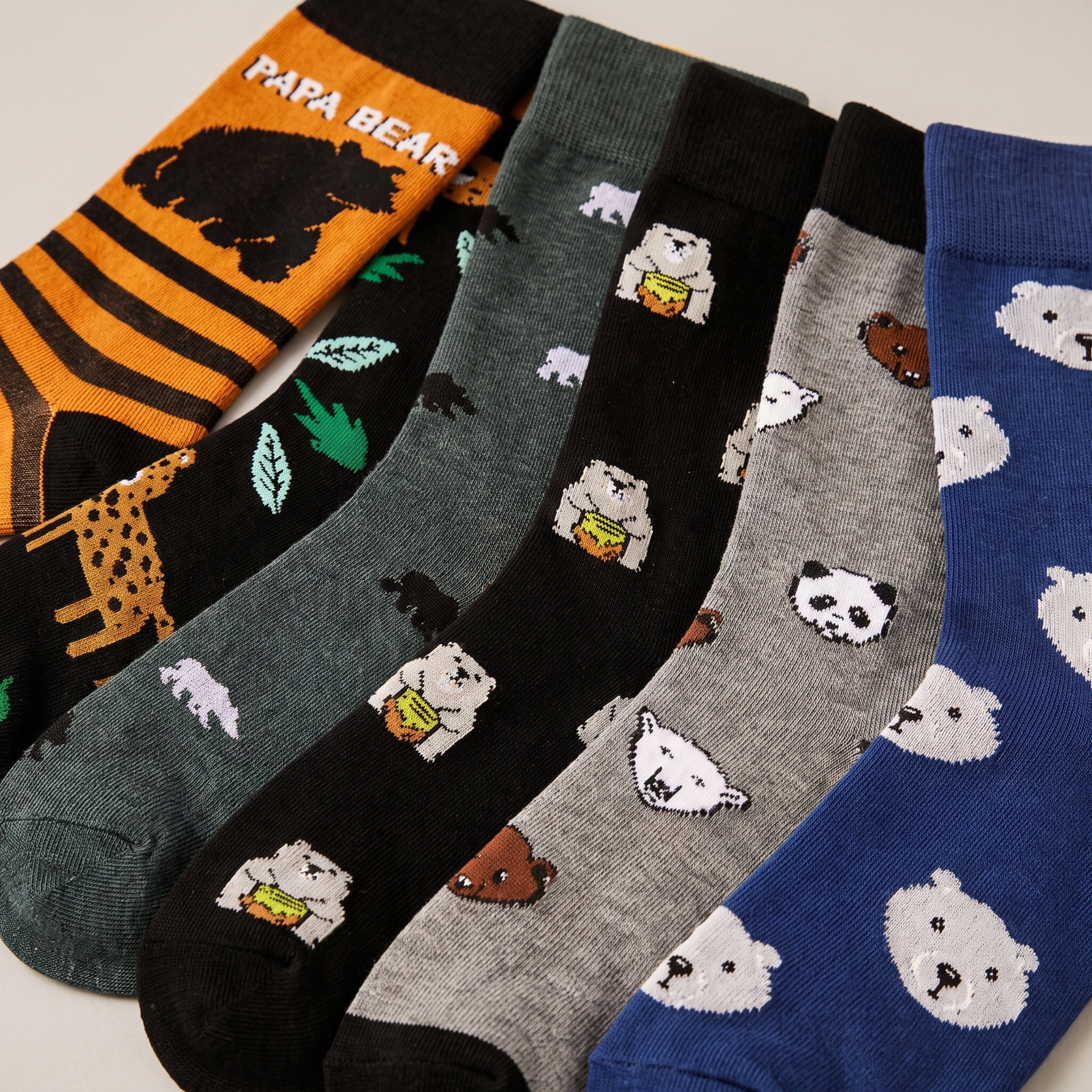 Six pairs of novelty socks arranged in a fan layout, featuring cute cartoon polar bear designs on various colors and patterns including stripes, leopard print, and solid blue.