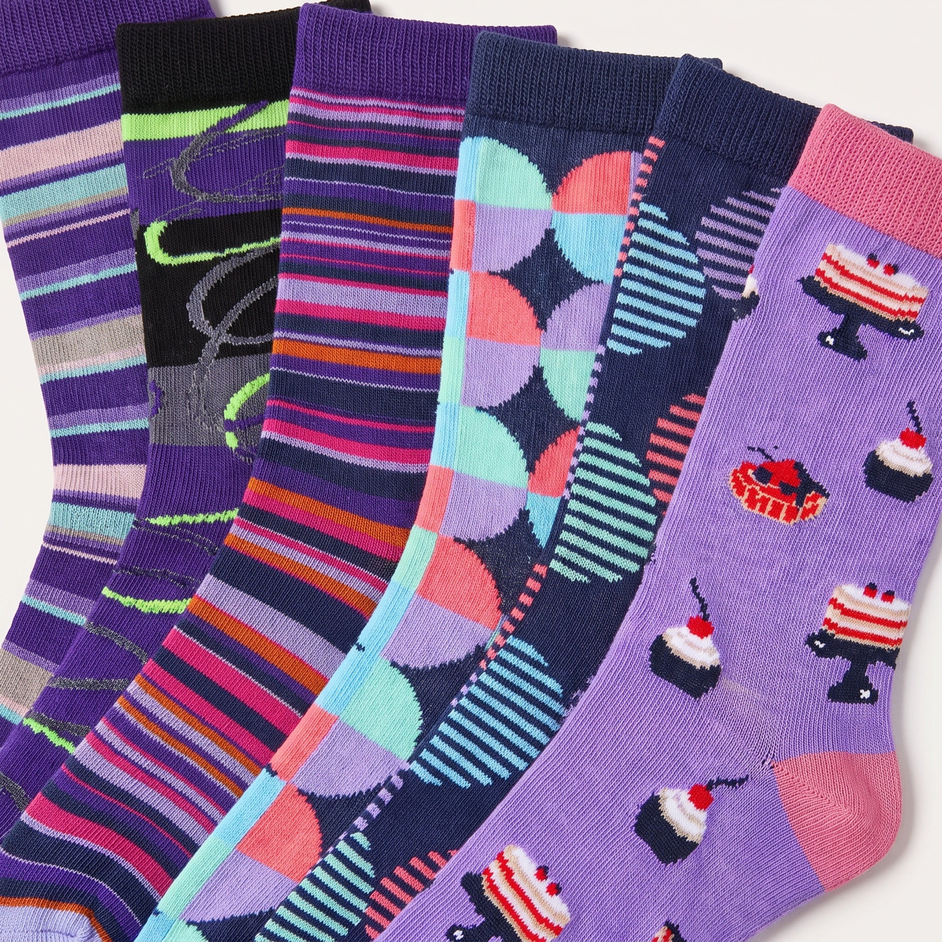 Six pairs of colorful patterned socks fanned out on a white background. The designs include stripes, abstract shapes, and cupcake motifs in purple, pink, blue, orange, and black.