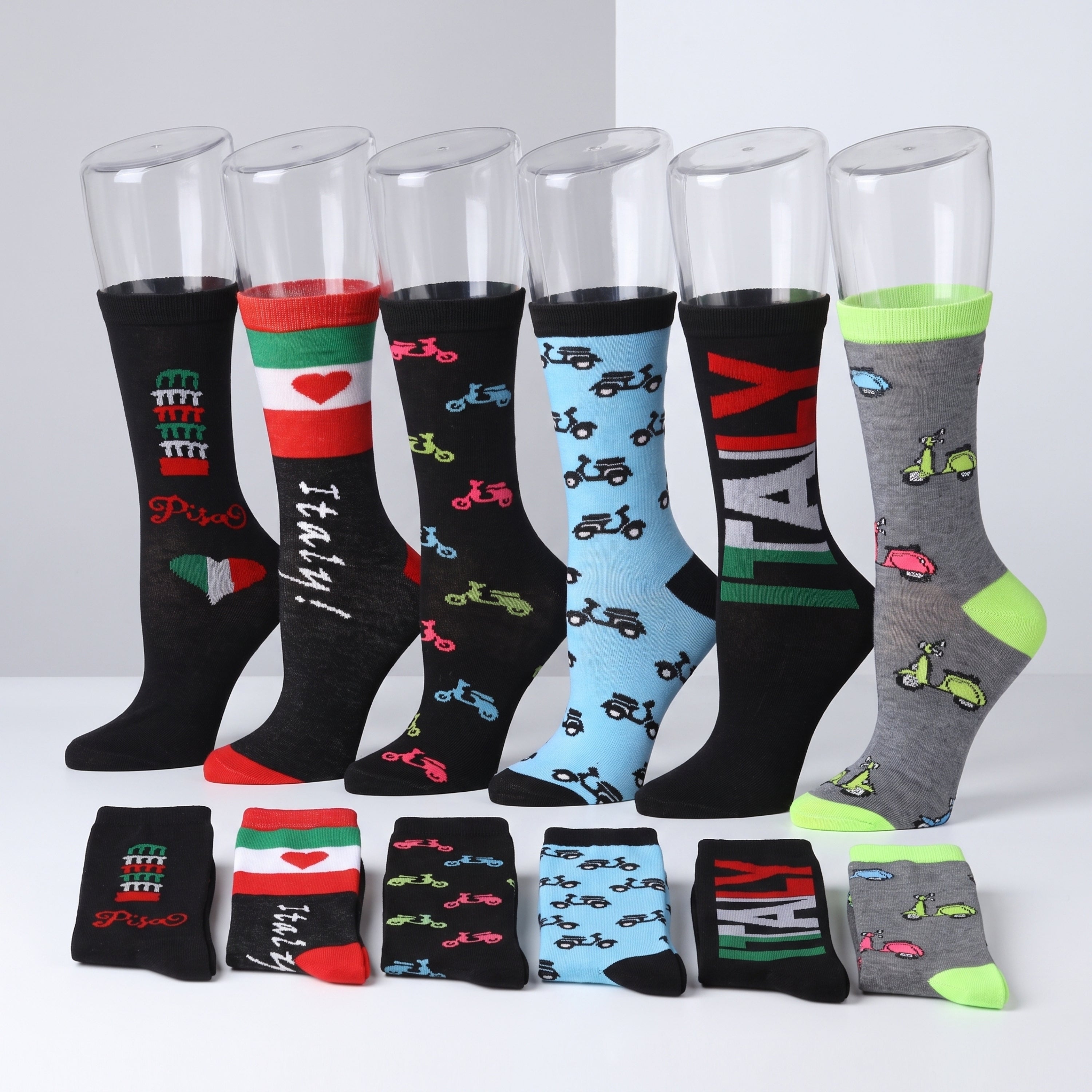 Six pairs of novelty crew socks displayed on clear plastic mannequin legs, with four additional pairs folded in front. The socks feature colorful Italian-themed prints including bicycles, the Italian flag, a tower, and the word 'ITALY'.