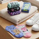 Stack of folded towels with text and designs, next to a pair of white sneakers on a wooden surface.
