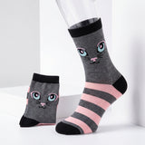 A pair of gray crew socks with a cute cartoon cat face and pink and black stripes, displayed on a white studio background with one sock on a mannequin leg and the other standing beside it.