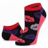 A pair of low-cut ankle socks on a white background. The socks feature a black knit base with a pattern of red, pink, purple, and gray lipstick kiss marks, accented with red ribbed cuffs, purple side panels, and pink heels.