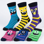 Six pairs of colorful monster-themed crew socks arranged on a light gray background. The socks feature bold horizontal stripes and cartoon monster faces in blue, yellow, purple, pink, blue, and green.