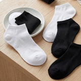 White and black socks on a wooden surface with a small white dish.