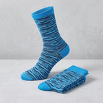 A pair of bright blue crew socks with a dark navy blue wavy stripe pattern, with one sock standing upright and the other folded on a light gray surface.
