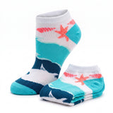 A pair of low-cut ankle socks with a beach-themed pattern featuring turquoise waves, white sand, a dark blue shoreline, and coral starfish, shown on a clean white background.