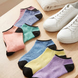 Colorful socks with black toes and heels on a wooden surface next to white sneakers.