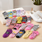A set of colorful cartoon-patterned ankle socks arranged on a light wood surface next to a white towel and white sneakers. The socks feature various designs including bees, bunnies, lions, hearts, and text like 'Happy Bunny', 'Honey', and 'Princess'.