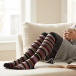 Person wearing striped socks sitting on a couch with a cup and book, brand 'TipiToe' visible