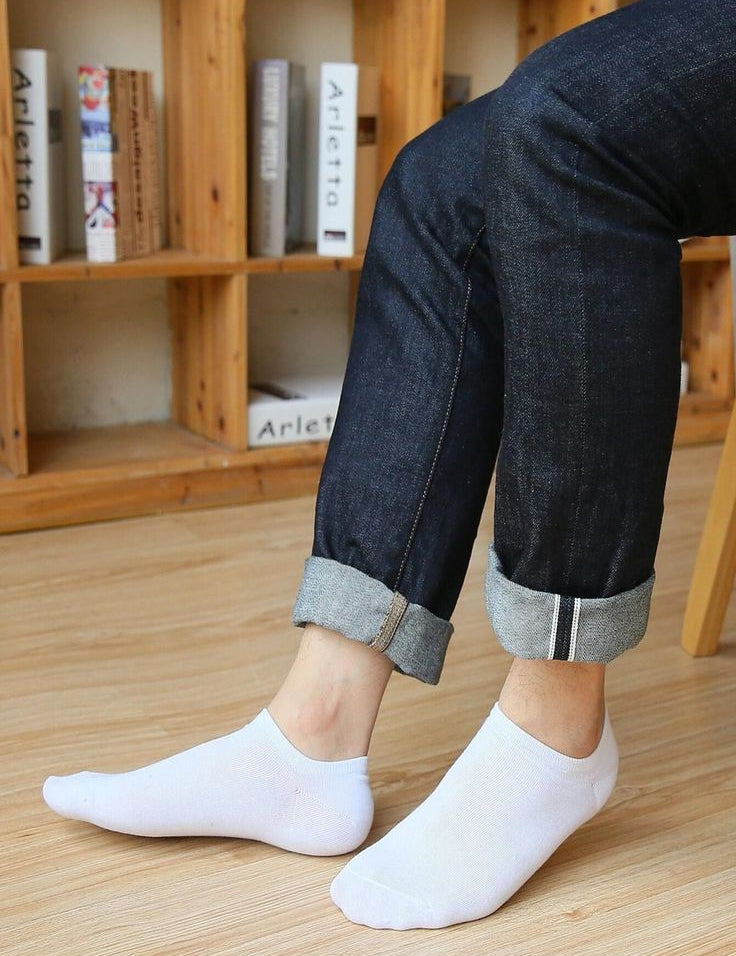 Person wearing dark jeans with rolled-up cuffs and white socks on a wooden floor.