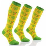 Three knee-high socks with a bright yellow background, green leaf and flower pattern, and solid green cuffs, heels, and toes, displayed on a white reflective surface.