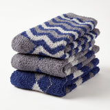Three folded plush bath towels stacked on a white background, featuring a blue, gray, and white chevron pattern.