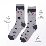 A pair of crew socks with a gray and navy cat face pattern, black paw prints, and small red and beige spots, shown on a white background with feature callout text and icons.
