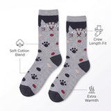 A pair of crew socks with a gray and navy cat face pattern, black paw prints, and small red and beige spots, shown on a white background with feature callout text and icons.