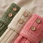 Three close-up views of knitted sleeve cuffs in olive green, cream, and dusty pink, each with four round wooden buttons on a soft beige fabric background.