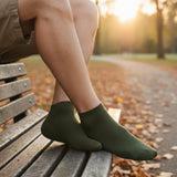 Person wearing green socks sitting on a wooden bench in a park with a blurred autumn background.