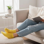 Person wearing yellow socks and blue jeans sitting on a couch with a tablet.