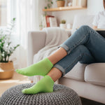 Person wearing bright green socks and blue jeans sitting on a ottoman in a living room.