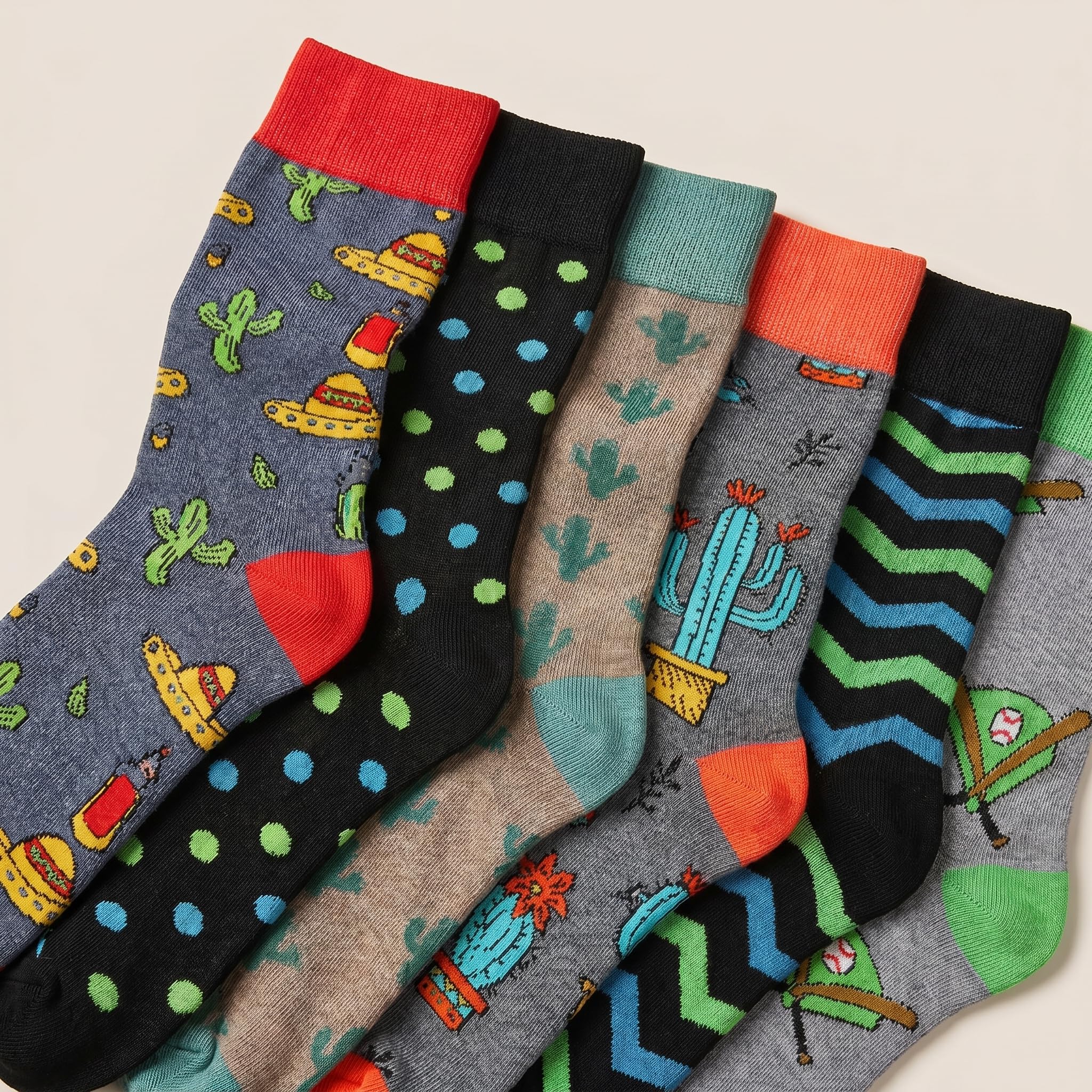 Six pairs of patterned crew socks arranged overlapping on a light beige background. The socks feature various colorful designs including cacti, chevron stripes, polka dots, and sombrero motifs in gray, black, beige, teal, green, orange, and red.