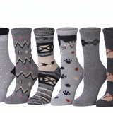 Six pairs of patterned crew socks displayed side by side against a plain white background. The socks feature various designs including snowflakes, geometric patterns, animal motifs, and argyle, in shades of gray, black, and beige.