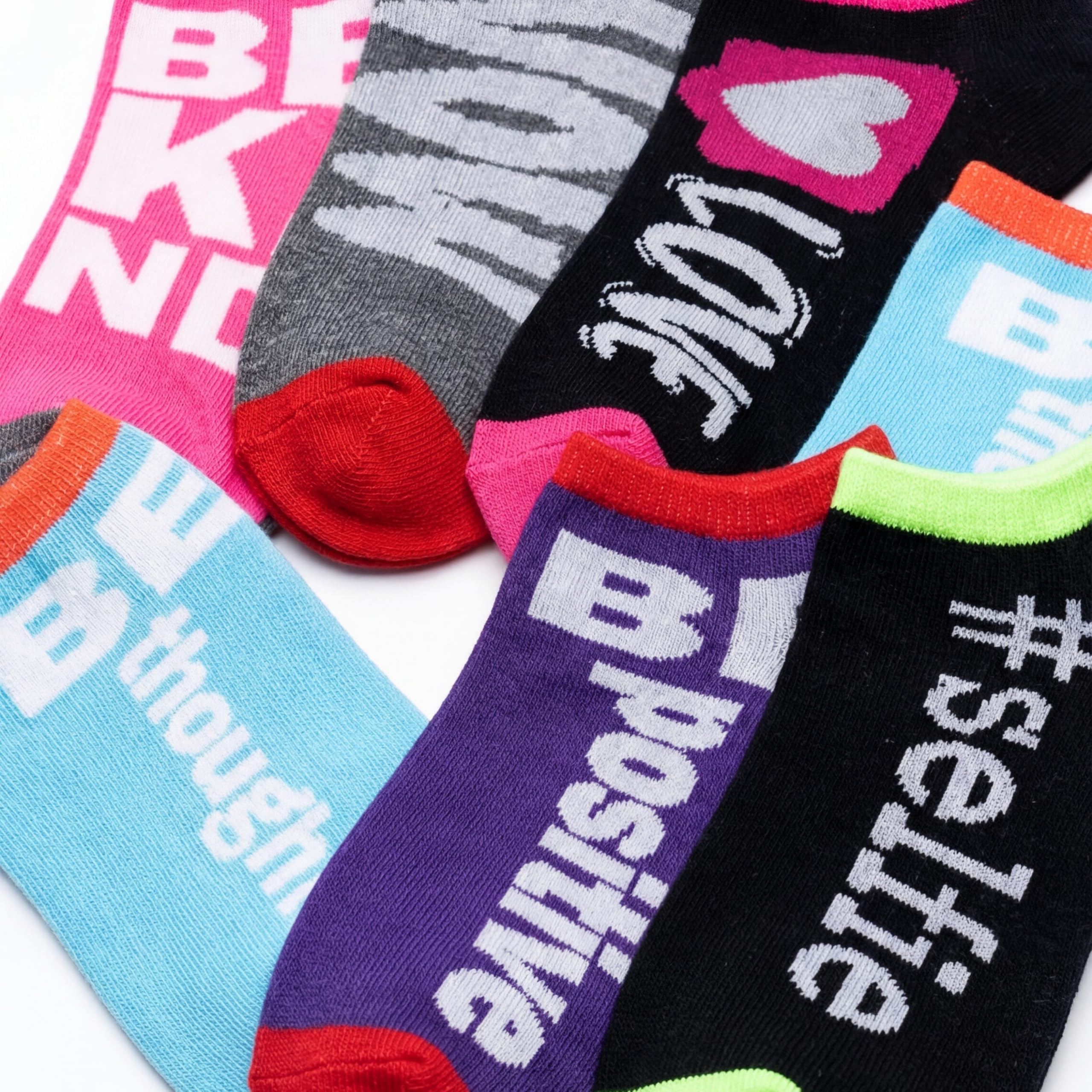 A close-up flat lay of several colorful novelty socks with bold text and graphic prints, including phrases like 'BE KIND,' 'I LOVE U,' 'thoughtful positive,' and '#selfie.'.
