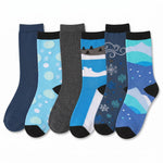 Six pairs of children's crew socks arranged in a fan shape on a white background. The socks feature various winter-themed patterns including snowflakes, snow caps, and mountain landscapes in shades of blue, gray, and black.