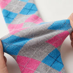 A close-up of a hand stretching a gray knit sock with a pink and blue argyle pattern, showing its elasticity against a plain white background.