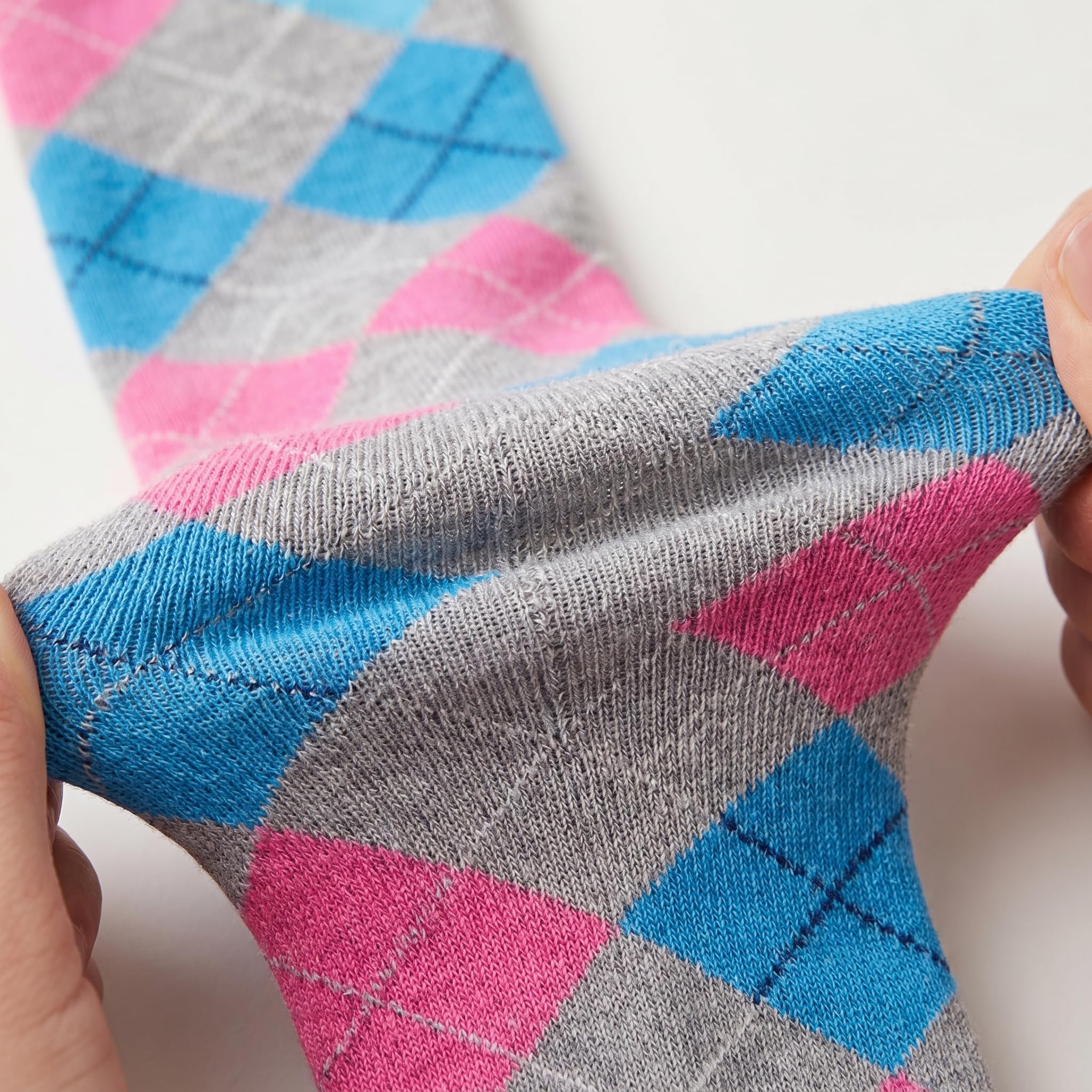 A close-up of a hand stretching a gray knit sock with a pink and blue argyle pattern, showing its elasticity against a plain white background.