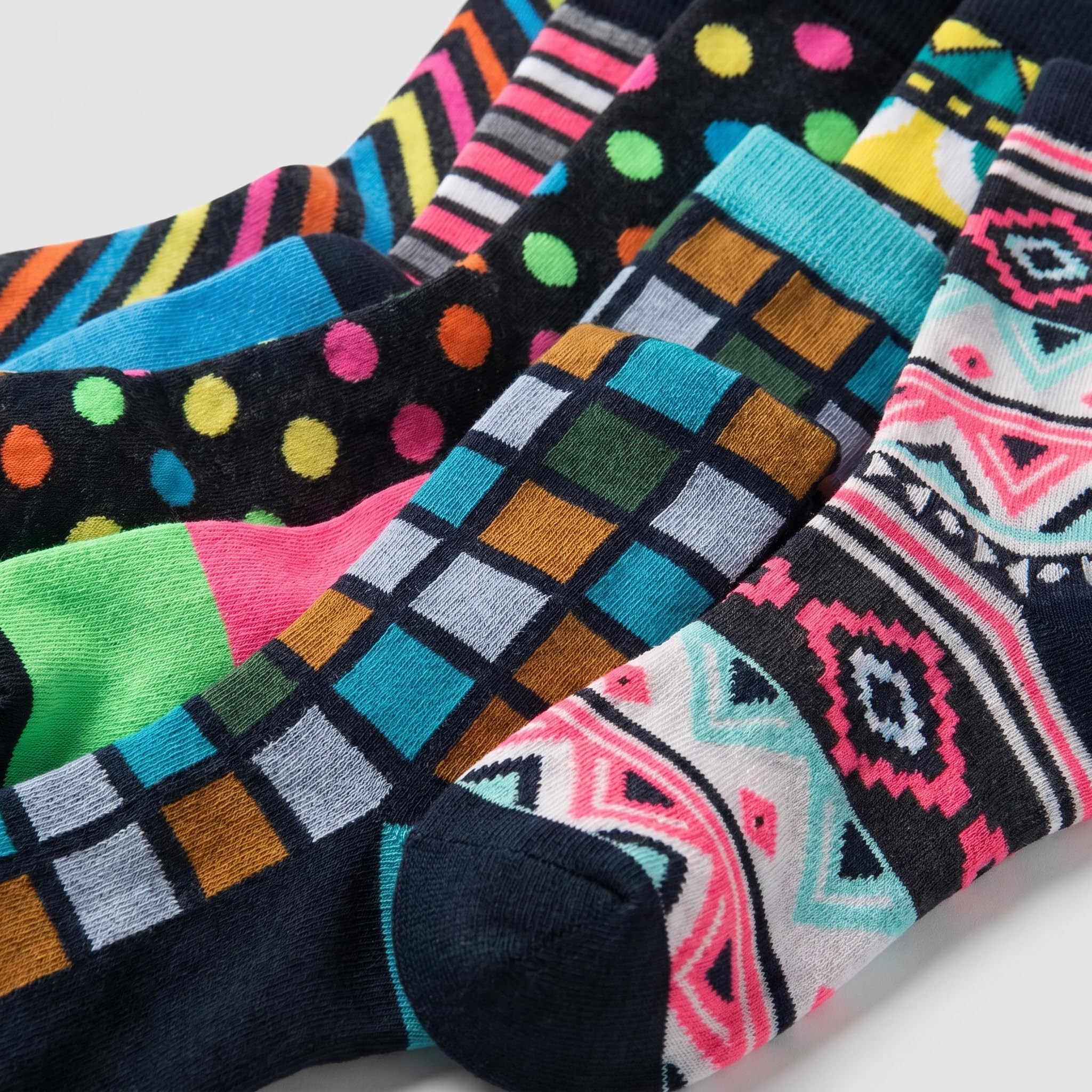 A close-up of several colorful patterned socks arranged diagonally. The socks feature various designs including polka dots, stripes, plaid, and geometric tribal patterns in black, pink, blue, green, yellow, orange, and white.