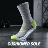 A gray athletic crew sock with bright green toe and heel accents, shown standing on a dark gym floor with a transparent sole graphic and the text 'CUSHIONED SOLE' at the bottom.