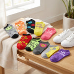 A set of colorful ankle socks arranged on a wooden bench next to white sneakers, with a cream towel draped over the bench in a bright indoor setting.