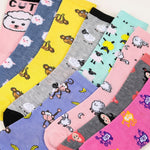 A set of colorful baby socks with playful cartoon prints, arranged diagonally. The socks feature various patterns including sheep, monkeys, bananas, and cute faces in bright colors like pink, yellow, blue, purple, and gray.