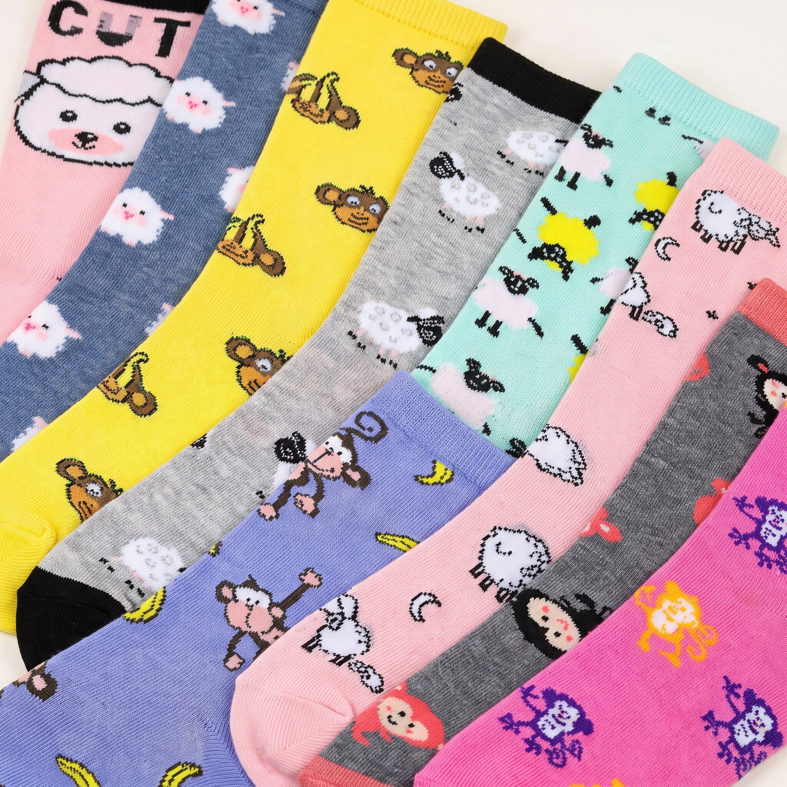 A set of colorful baby socks with playful cartoon prints, arranged diagonally. The socks feature various patterns including sheep, monkeys, bananas, and cute faces in bright colors like pink, yellow, blue, purple, and gray.