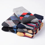 A stack of folded men's dress socks in various colors and patterns, including argyle and striped designs, on a clean white background.