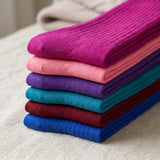 A stack of folded ribbed knit socks in multiple colors, including magenta, pink, purple, teal, burgundy, and blue, arranged on a light beige fabric surface.