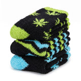 A stack of three folded plush socks on a white background. The socks feature a black base with lime green leaf-like patterns on the top and middle, and light blue accents on the toe and heel of the bottom sock.