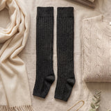 Black knee-high socks on a light surface with a beige scarf, books, and sweater.