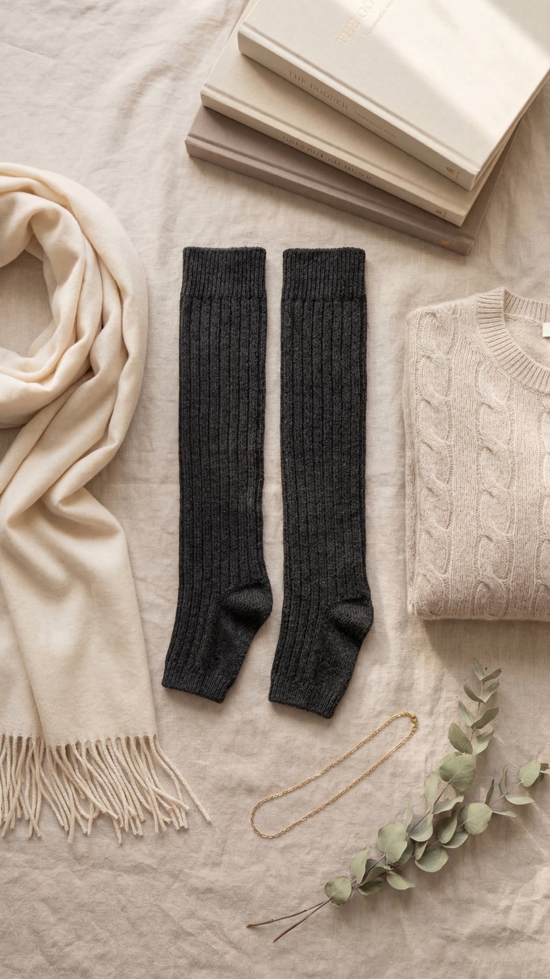 Black knee-high socks on a light surface with a beige scarf, books, and sweater.