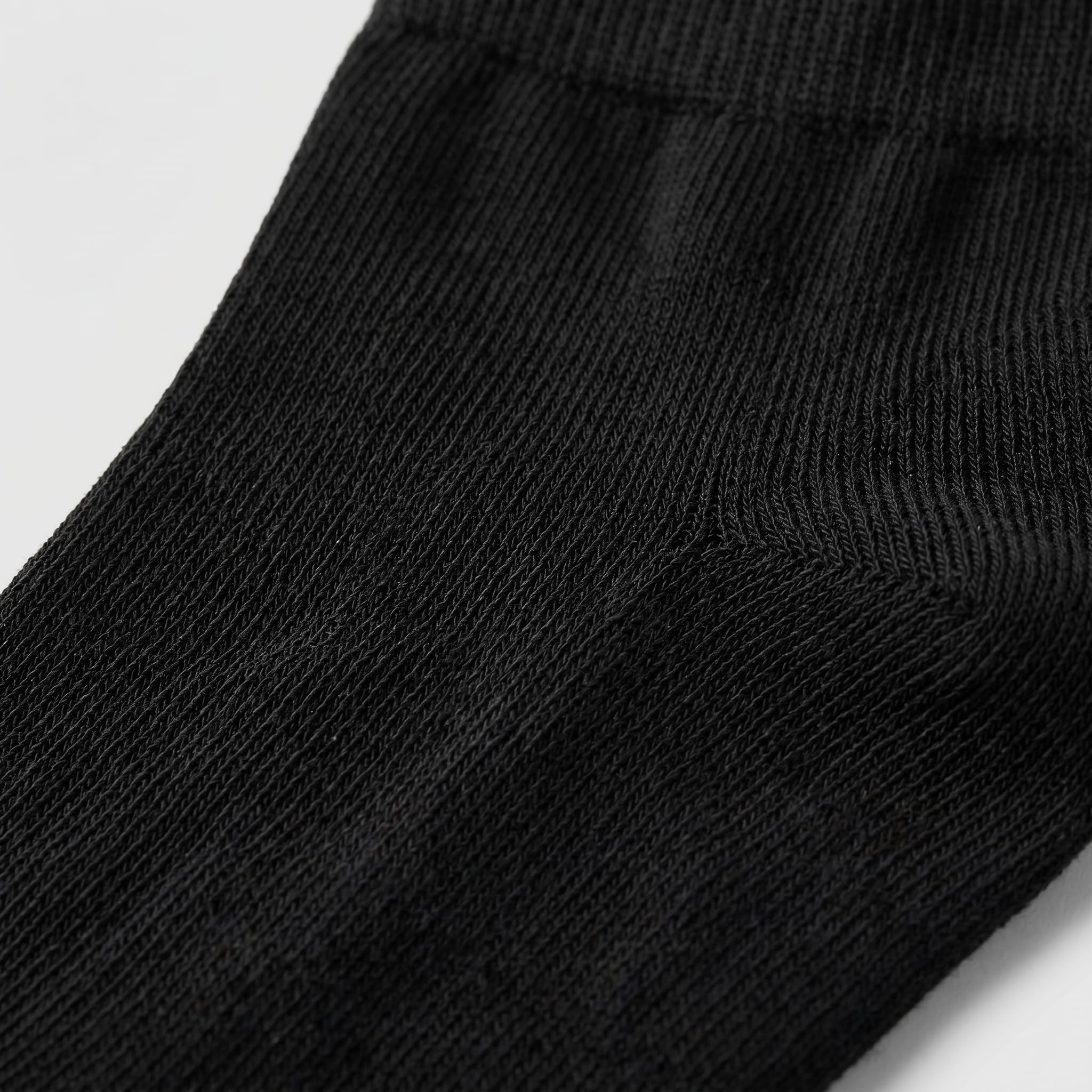 Close-up of a black ribbed knit sock showing the texture and cuff detail against a light gray background.