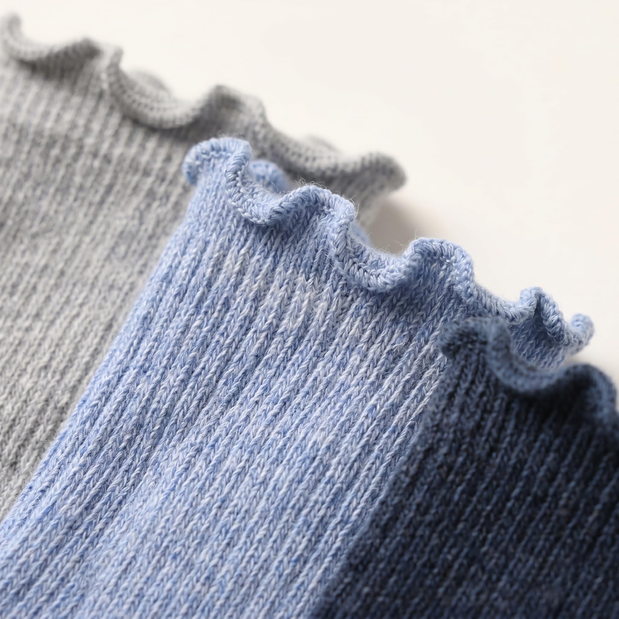 Close-up of ribbed knit socks with ruffled edges in soft blue and gray tones on a light neutral background.
