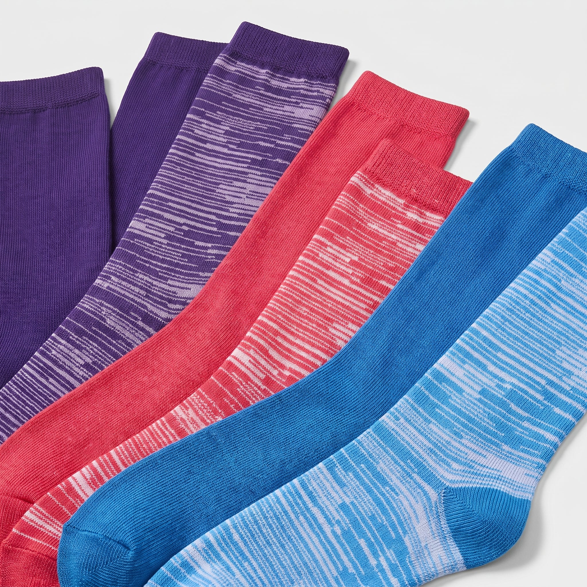 Four pairs of crew socks arranged diagonally on a light gray background, showing different colorways: solid purple, purple with white streaks, coral red with white streaks, and blue with white streaks.