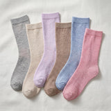 Five pairs of ribbed crew socks in soft neutral and pastel colors, arranged in a fan shape on a light fabric background. The colors are gray, beige, lavender, taupe, light blue, and pink.
